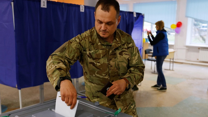 A man in military uniform casts his ballot at a polling station.