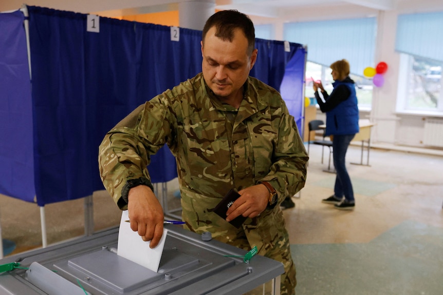 Un homme en uniforme militaire vote dans un bureau de vote.