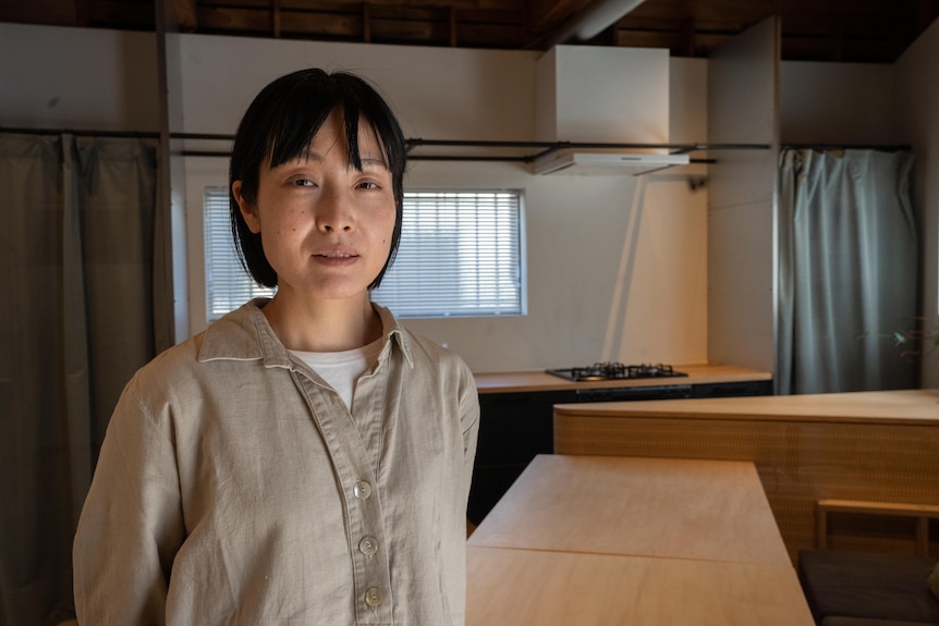 Saori Gunji looking at the camera in a room with a window behind her and desks 