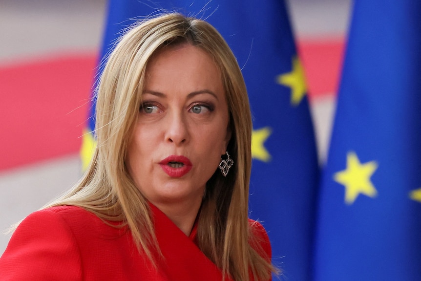 a closeup of Meloni's face as she stands in front of EU flags