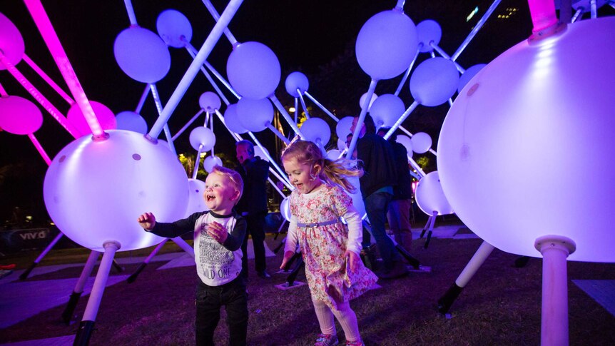 Two young children play among a white light installation.