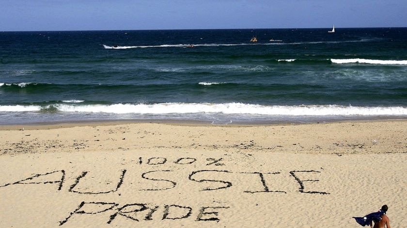 A man wearing an Australian flag walks past a slogan etched into the sand on Cronulla Beach