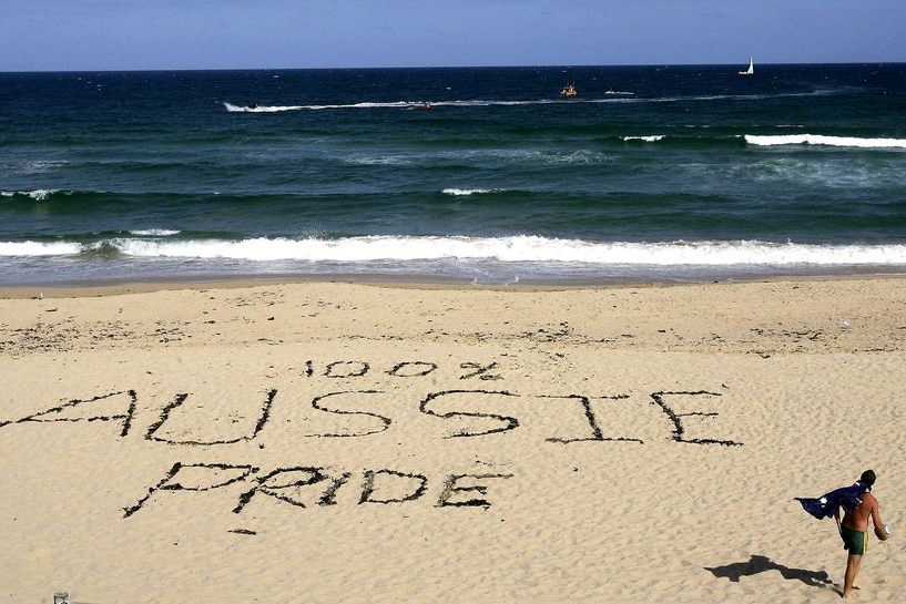 A man wearing an Australian flag walks past a slogan etched into the sand on Cronulla Beach