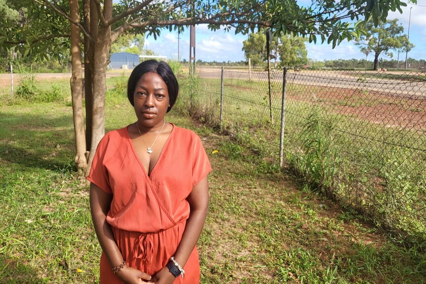 A woman in a red dress stands beside a fence.