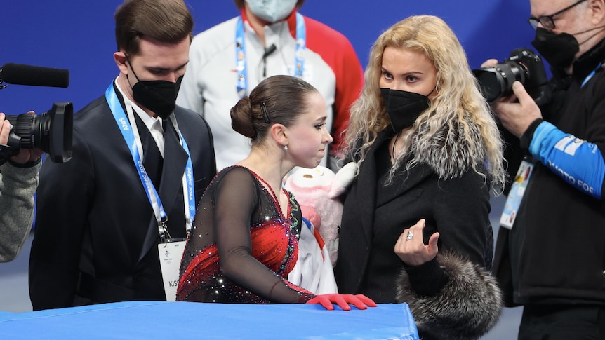 A girl walks off an ice rink as adults look on.