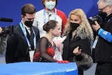 A girl walks off an ice rink as adults look on.