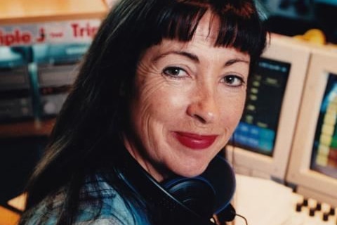 A woman sits in front of a radio panel in a studio