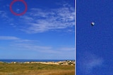 A small round object sits high in the sky above a beach with sand dunes in the foreground.