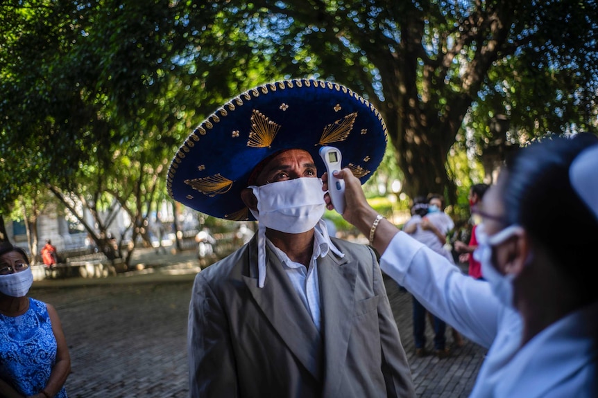 A nurse measures the temperature of a mourner wearing a Mexican hat in Havana, Cuba.