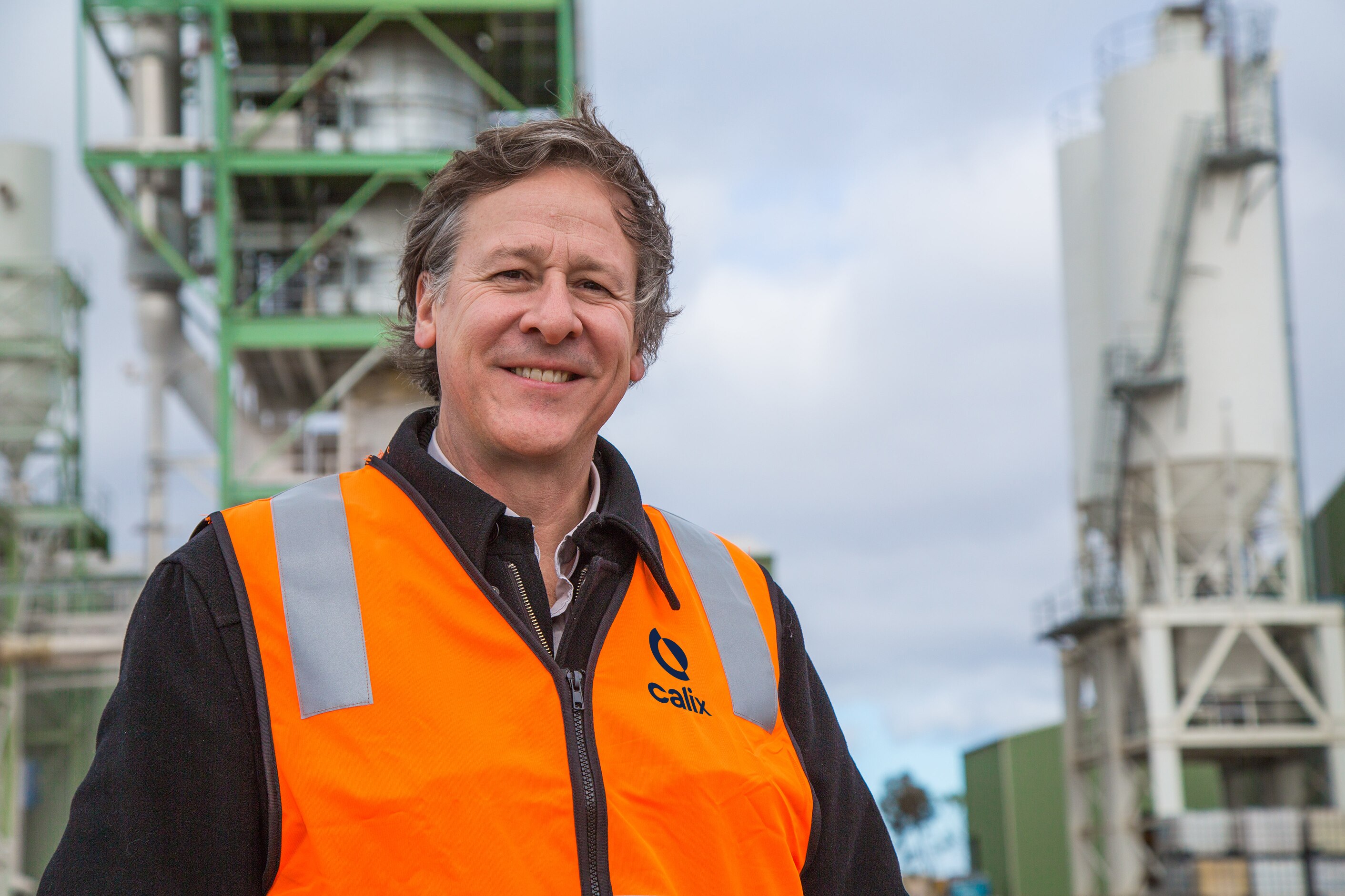 Um homem de colete posando para uma foto em uma instalação industrial