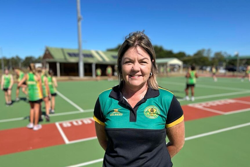 A woman standing on a netball court with a club shirt on.