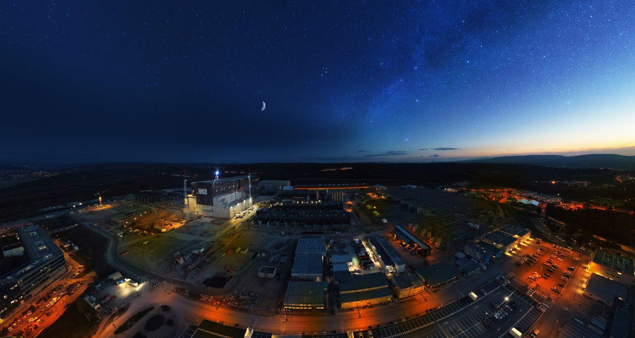 An aerial fish-eye lens shot showing the complex lit up, a crescent moon in the sky, and night falling