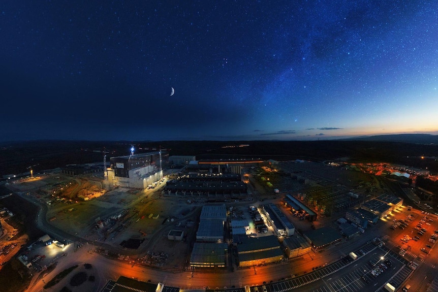 An aerial fish-eye lens shot showing the complex lit up, a crescent moon in the sky, and night falling