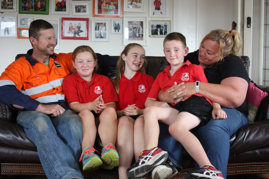 Greg and Traci Grogan sit on a brown couch with their three children.