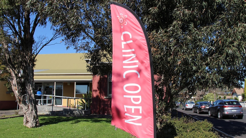 A red flag reading "clinic open" with a building and trees behind