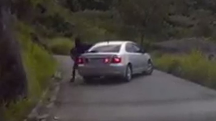 A dark figure gets out of a silver car blocking an Australian family from driving down a narrow road in Papua New Guinea.