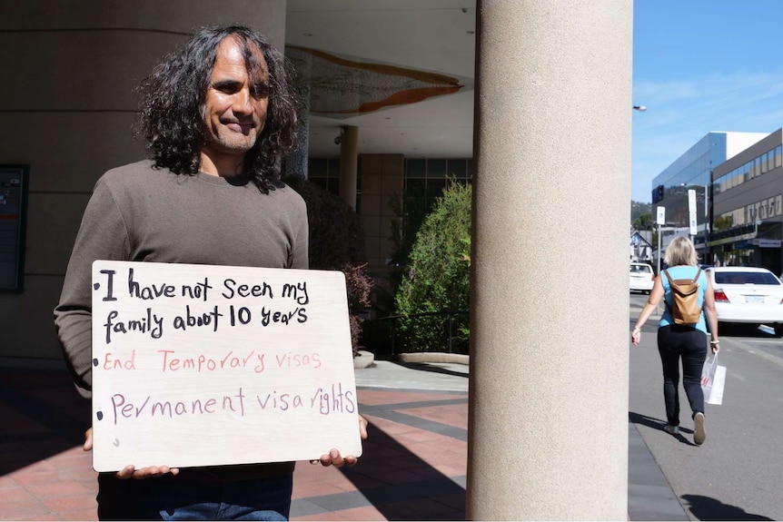 Photograph of a man holding a sign.