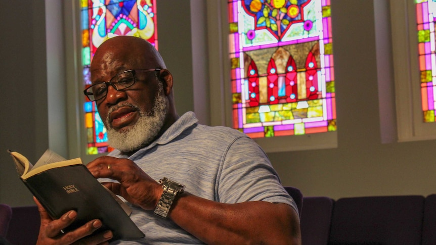 An African American man sitting in a church looking at the Holy Bible