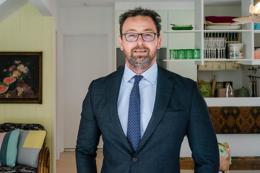 A man in a suit smiling inside a house