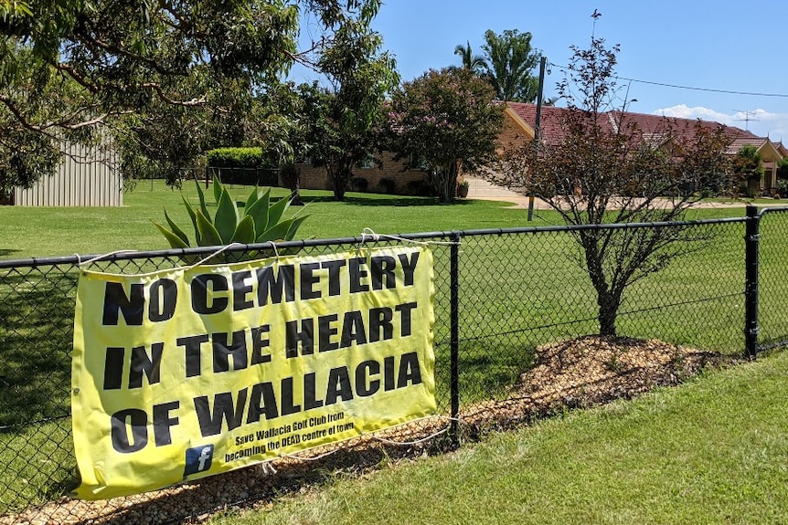 A banner hangs on a fence in front of a large green garden.