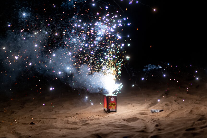 A firework explodes on the sand at the beach during the night on Territory Day.