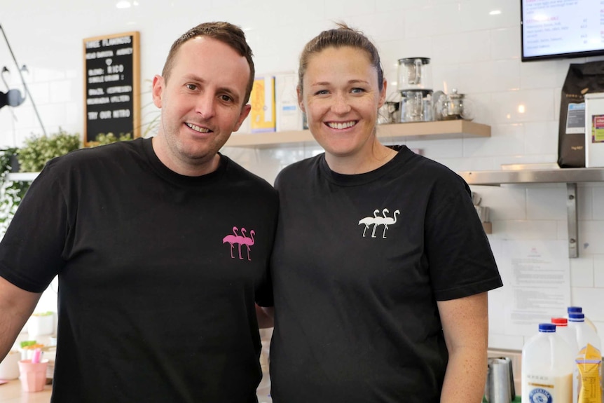 A man and woman stand in a cafe wearing black shirts.
