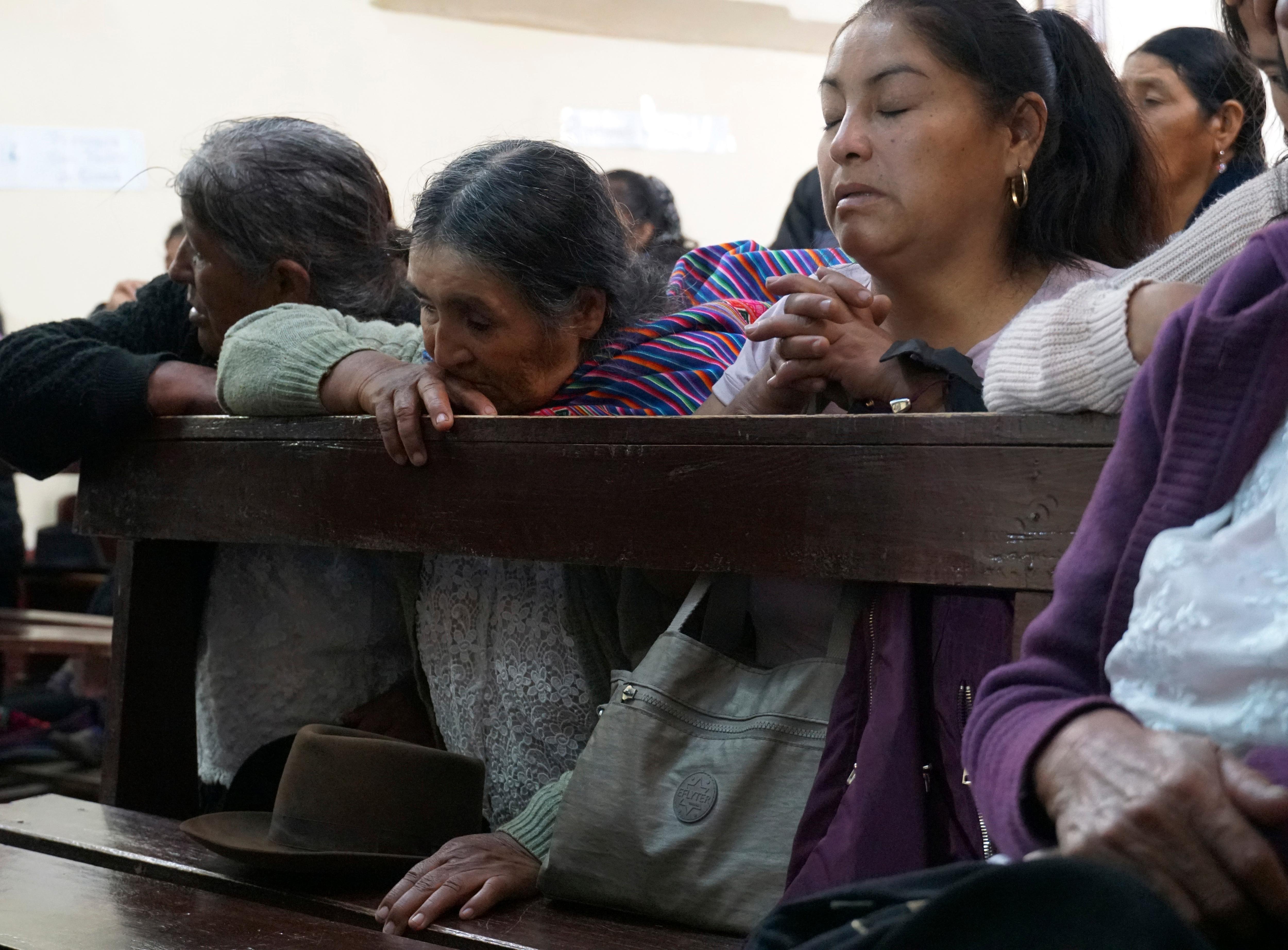 People pray on church pews. 