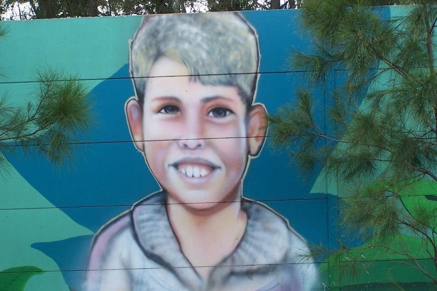 A large mural painting of a young boy with a toothy smile.