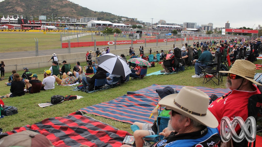 Crowds of people in supporter gear sit on a hill overlooking the Townsville 400 racetrack.