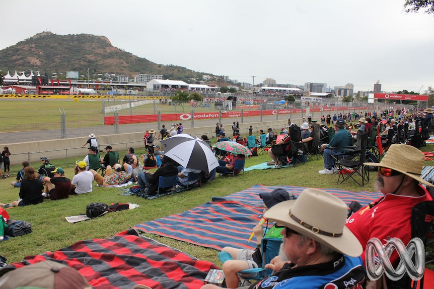 Crowds of people in supporter gear sit on a hill overlooking the Townsville 400 racetrack.