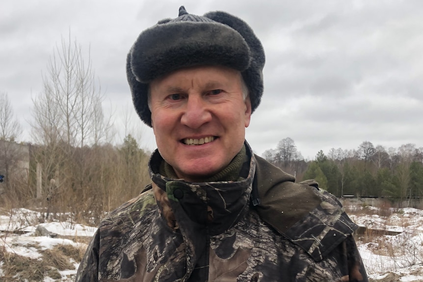 An older man in camouflage and a winter hat smiles for the camera.