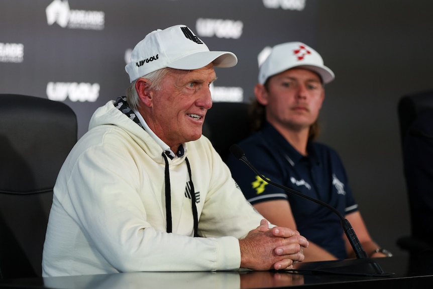 Two men sitting at a press conference wearing golf caps. 