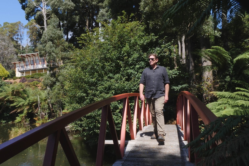 A man crosses a decorative walking bridge in a leafy garden.