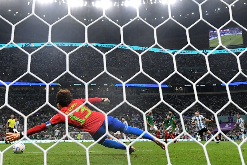 View from behind the goal as a Mexican goalkeeper dives and fails to stop a shot hitting the net, as the scorer is obscured. 