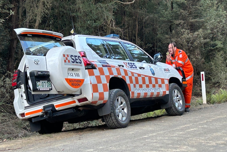 White and orange SES vehicle by the side of the road, with man leaning on bonnet.