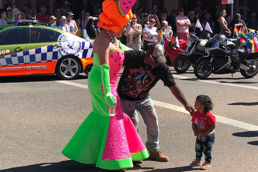 A drag queen dressed in a water melon themed costume greets a young Aboriginal child.