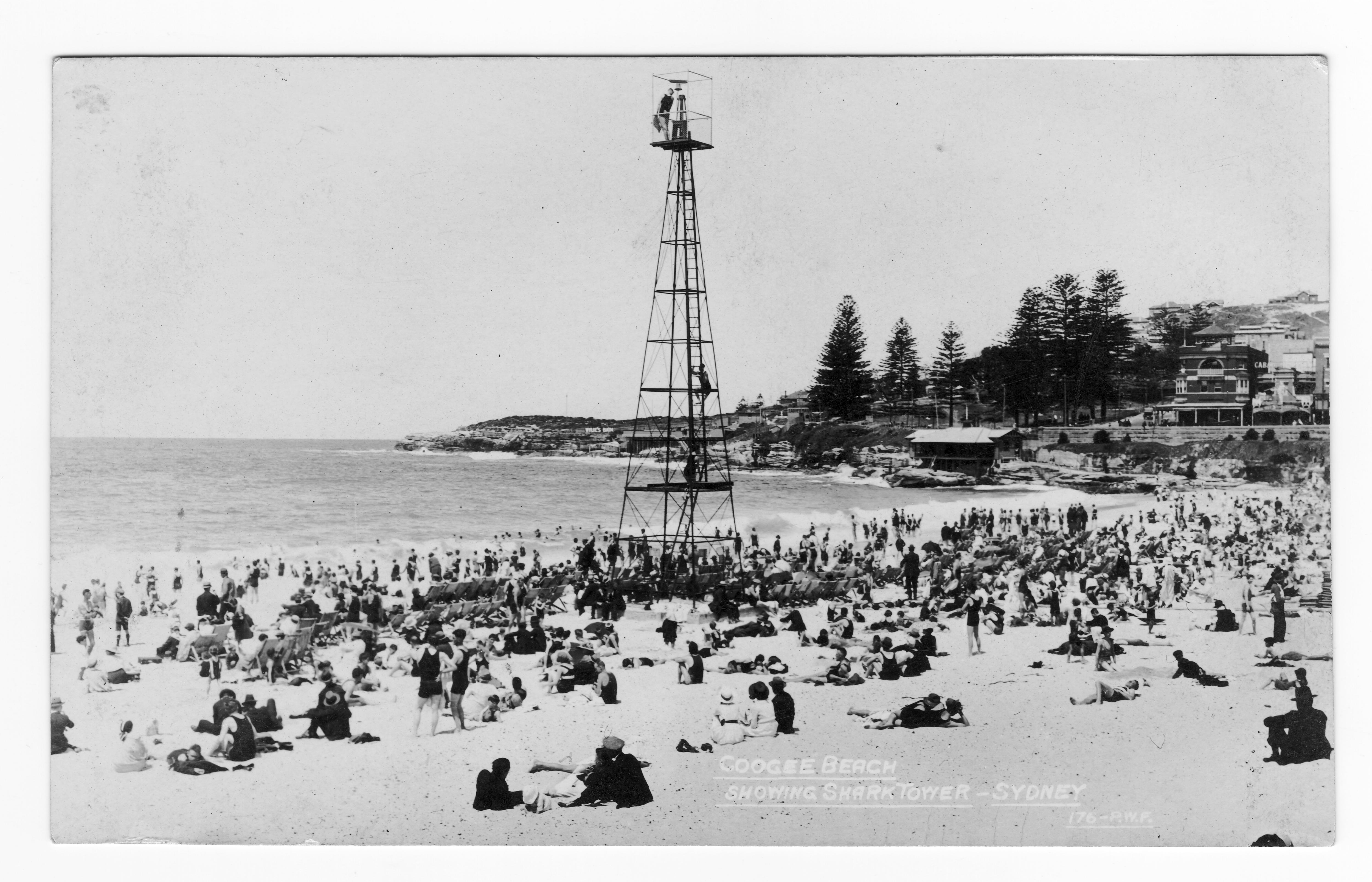 a tall thin tower on a beach full of beachgoers