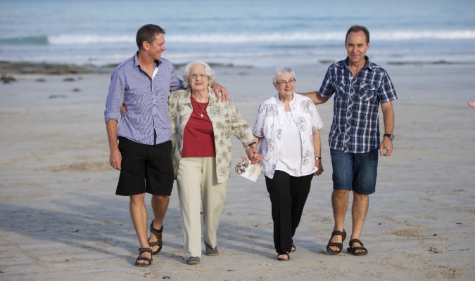 Two men and two women walk smiling along a beach
