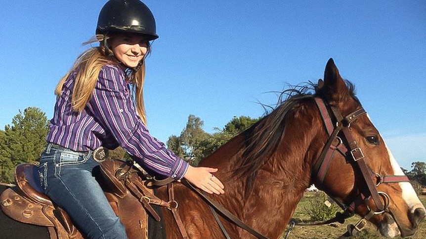 Young woman sits astride a horse, patting its flank