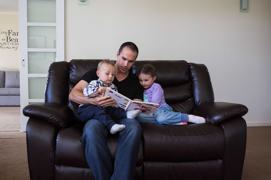 A man sits on a couch reading a story to two small children.