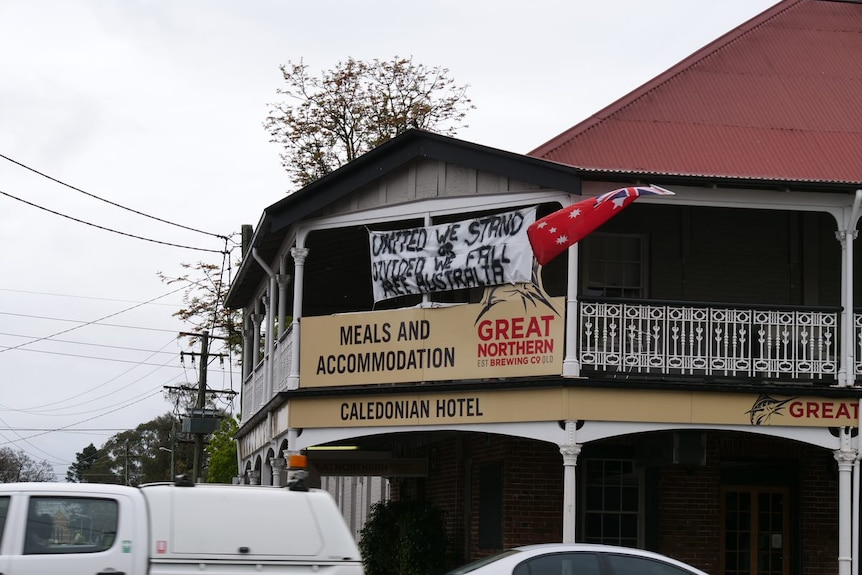 A sign hanging from a balcony reading 'united we stand, divided we fall, free australia'