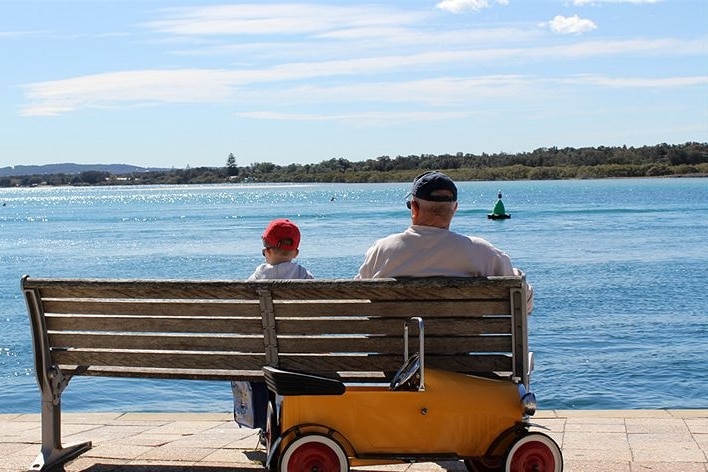 A man and his son sit on a bench overlooking a lake.