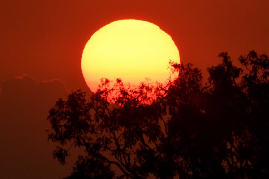 A close up of a bright orange sun in red sky.