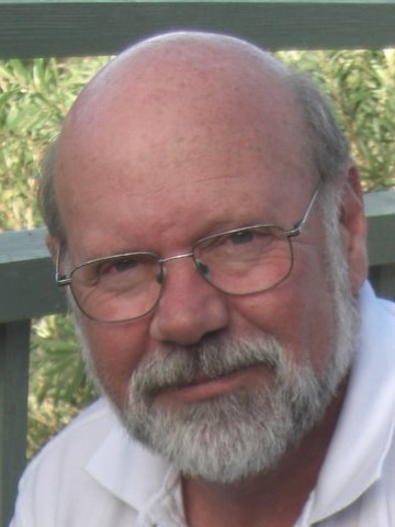 older man with beard, wearing reading glasses and polo smiles outside 