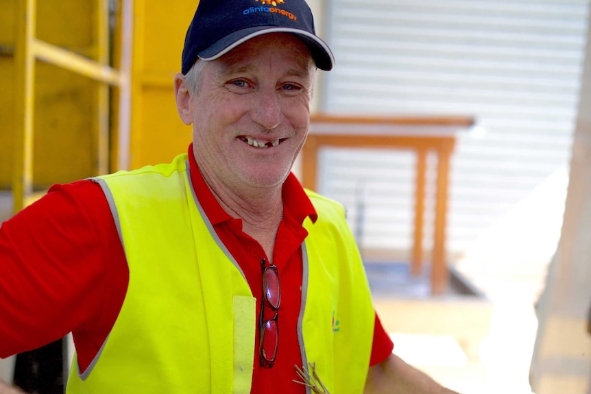 Ian Brown smiles at the camera holding a crate of vegetables and wearing a hi-vis vest.