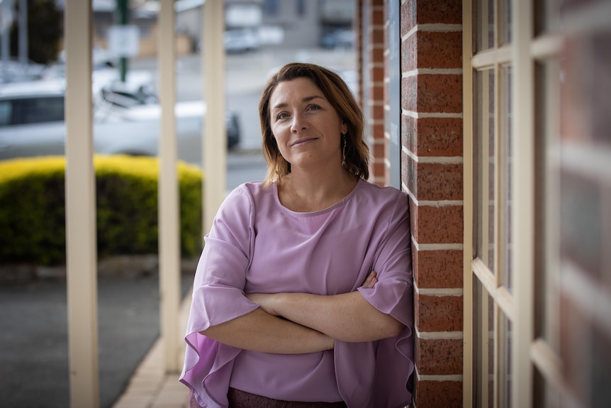 Dr Maddi Derrick wears a lilac top and leans against a brick wall outside her Bellerive clinic.