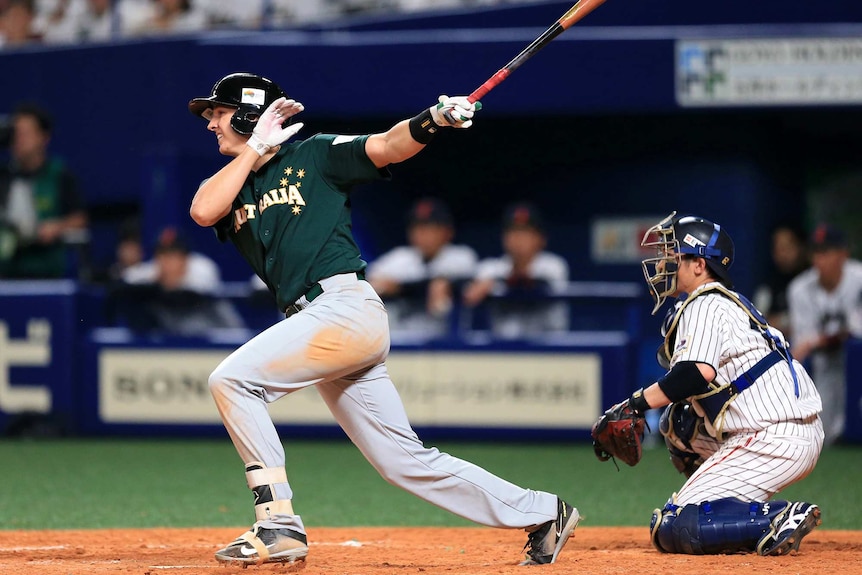 Baseballer Robbie Glendinning swings at bat watching the ball disappear with a catcher behind him.