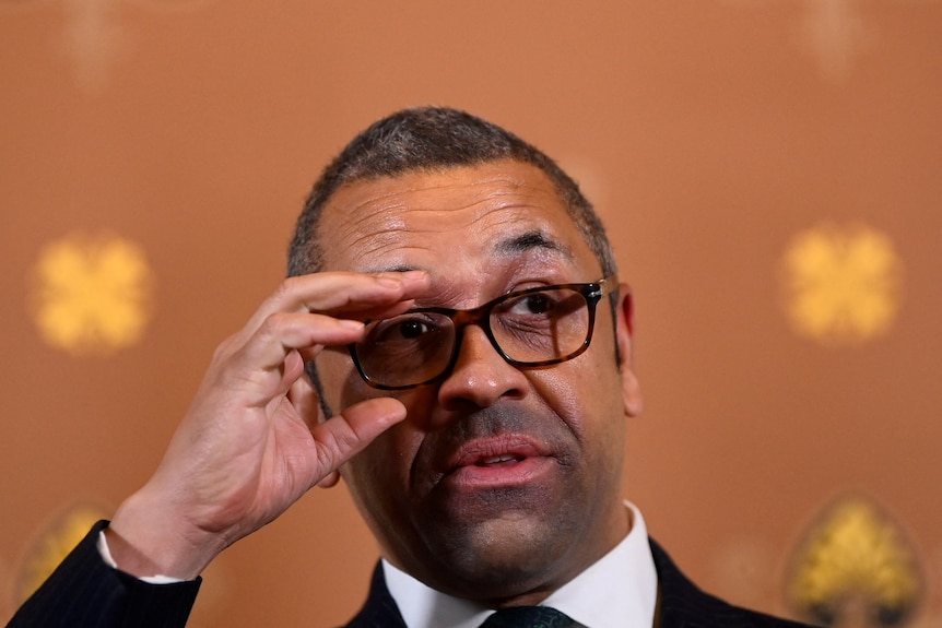 Close up of UK Foreign Secretary James Cleverly as he readjusts his glasses.