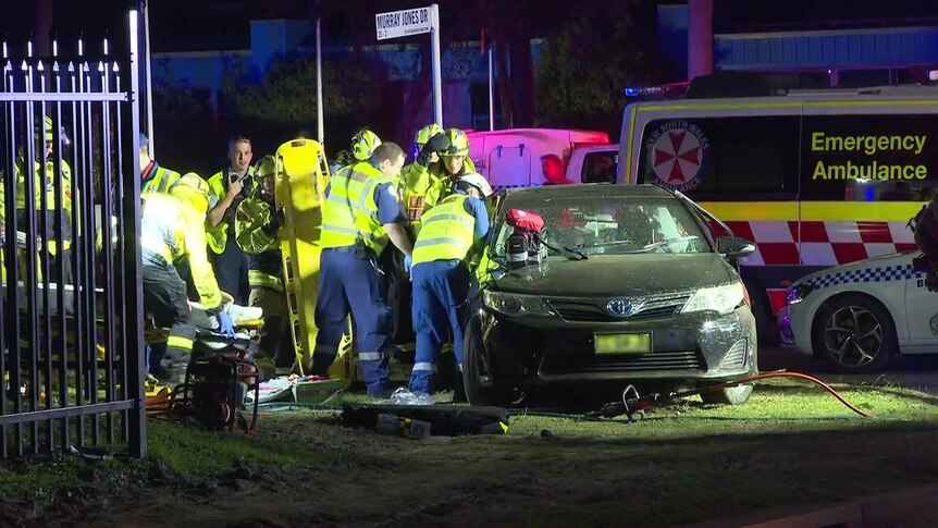 Emergency service workers work to pry open a smashed-up car involved in a multi vehicle crash at night.
