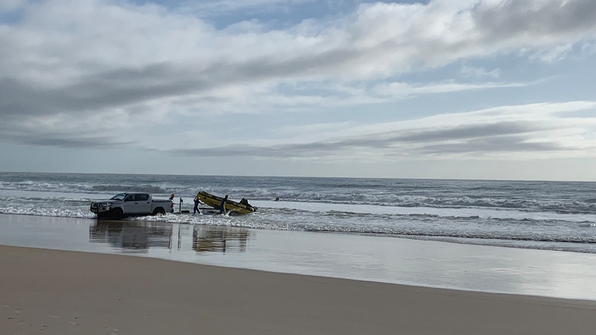 A car and a boat backing into to the ocean under a semi-blue sky.